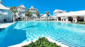 A large swimming pool surrounded by white buildings with balconies and palm trees. - Serene newly built island home with outdoor pool, beach boardwalk & on-site golf (Port Aransas)