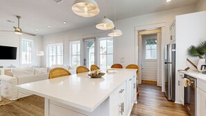 A spacious kitchen with a large island, white cabinetry, and modern pendant lighting. - Serene newly built island home with outdoor pool, beach boardwalk & on-site golf (Port Aransas)