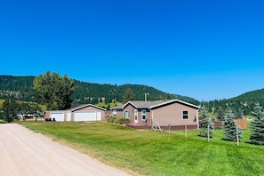 Houses with attached garages sit on a well-maintained lawn surrounded by rolling hills and dense forests.