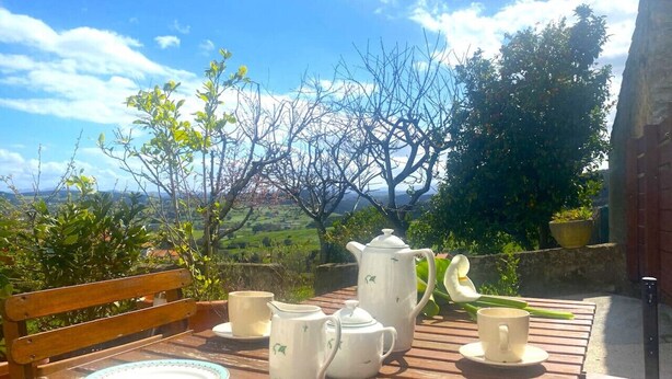 A wooden table with a teapot, cups, and saucers set outdoors with a scenic view in the background.