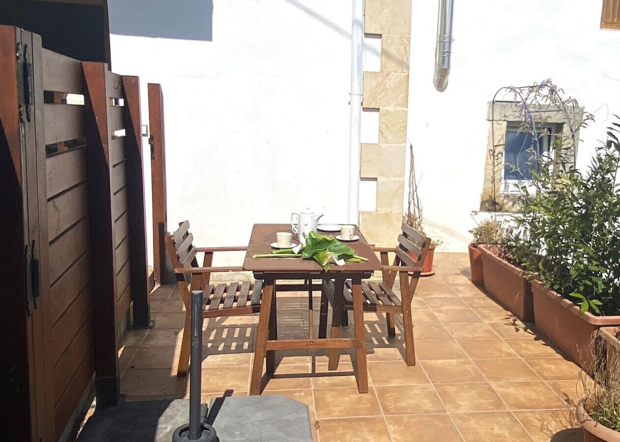 A patio with a wooden table and chairs, a tiled floor, and potted plants.