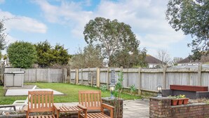 A patio with wooden chairs and a table, a brick planter with plants, and a wooden fence in the background. - 2 bedroom accommodation in Poole (Poole)