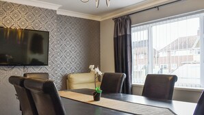 A dining area with a table, chairs, a television, and a window with curtains. - 2 bedroom accommodation in Poole (Poole)