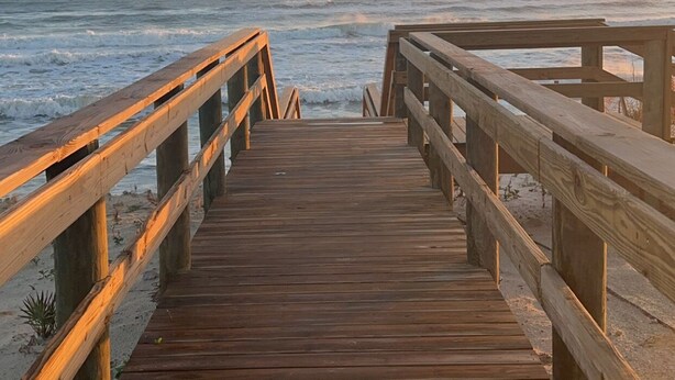 Ein hölzerner Promenadenweg führt zum Meer, der Himmel ist wolkenlos.