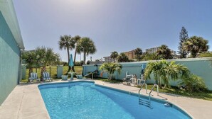 Ein Pool mit Liegestühlen und Sonnenschirm, umgeben von Palmen und einer niedrigen Mauer.