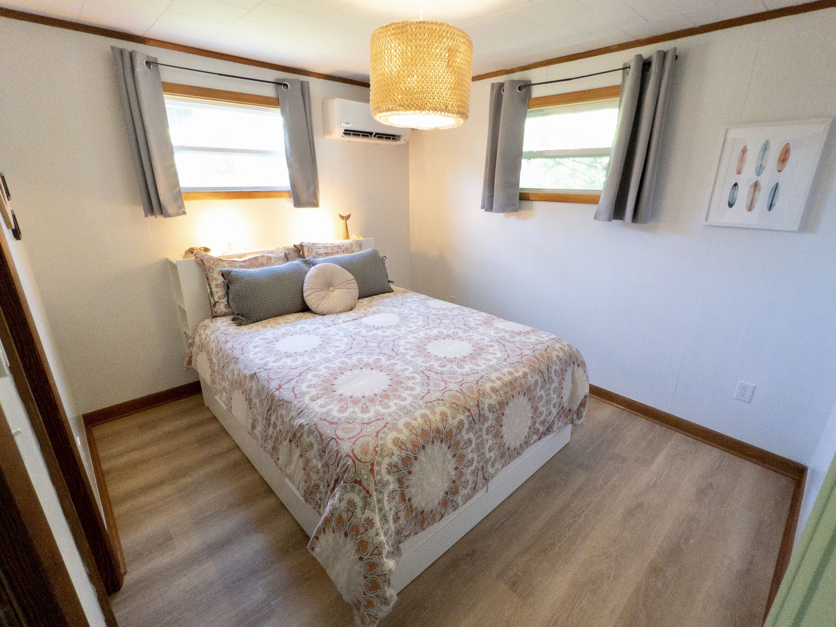 A bedroom with a bed, curtains, a hanging light fixture, and a wall-mounted air conditioner.