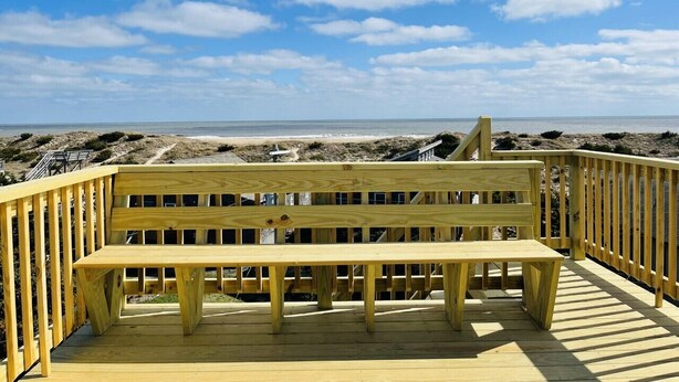 A wooden deck with a bench overlooking a beach.