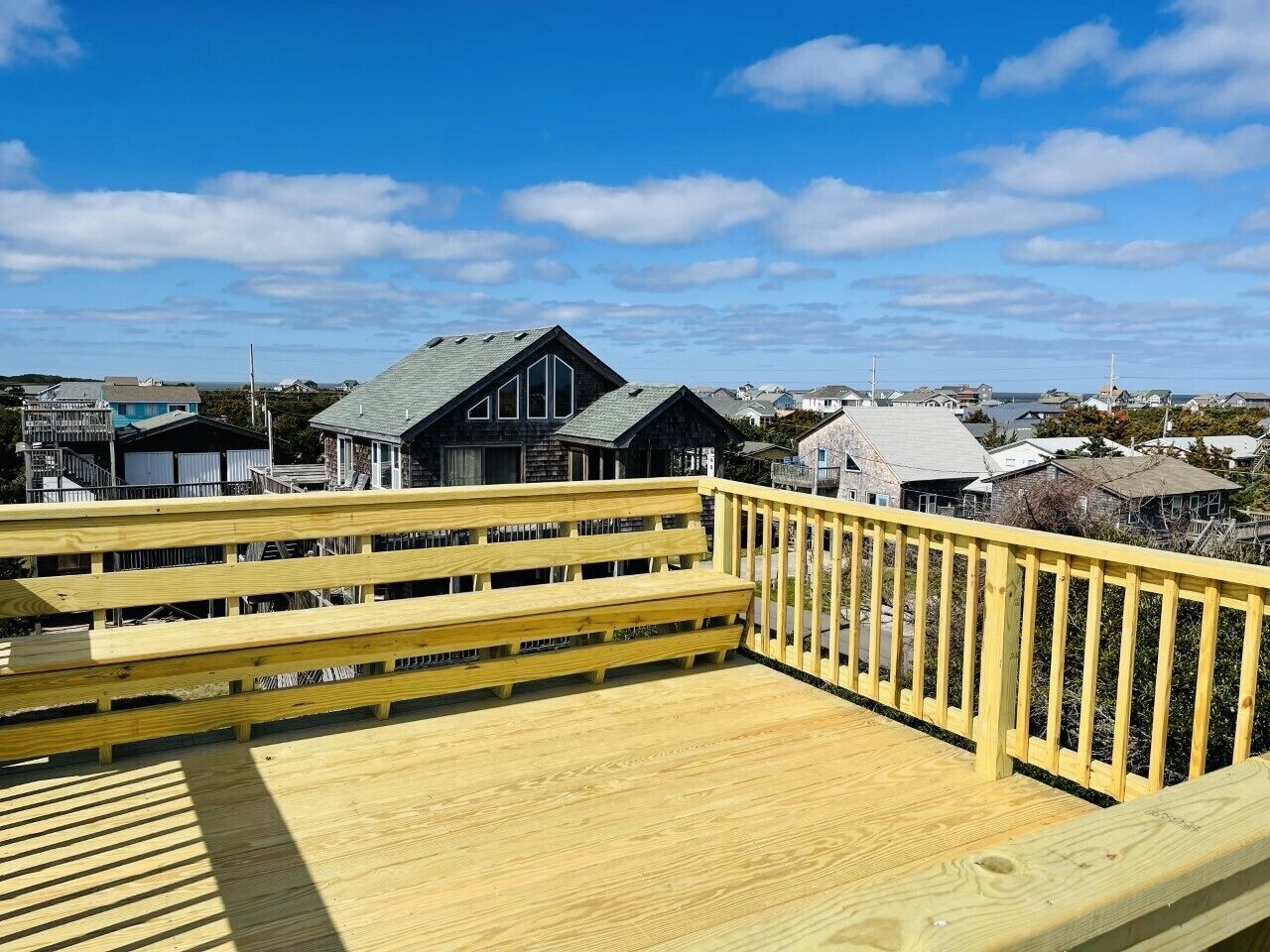 A wooden deck with benches and a railing, overlooking a residential area with houses and a clear sky.