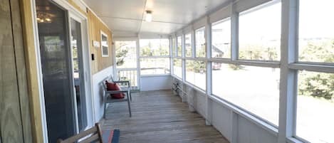 A covered porch with wooden flooring, a bench, and a chair.
