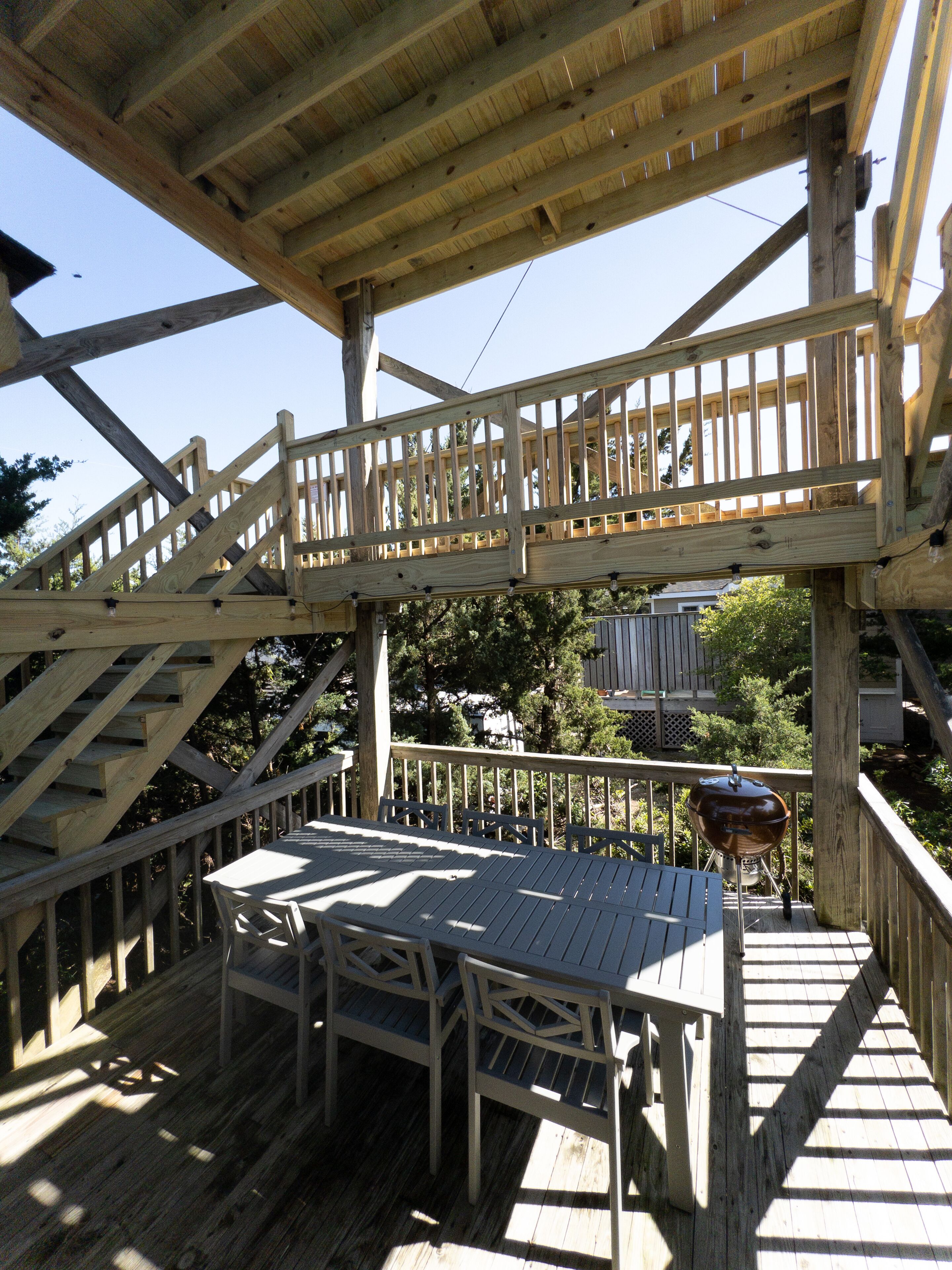 Une terrasse en bois avec une table et des chaises, un barbecue et un escalier menant à un niveau supérieur.