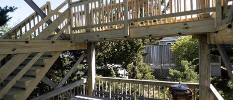 A wooden deck with a table and chairs, a barbecue grill, and a staircase leading to an upper level.