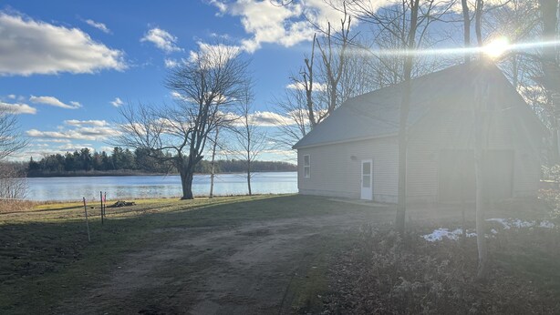 A house with a dirt driveway leading to a grassy area beside a lake. - Lake front Rustic Cabin in the UP, Snowmobile-ATV trails, Falls, Mackinaw Island (Trout Lake)