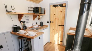 A compact kitchen with a central island, a stove, and a wooden door. - The Queen Bee (Pembroke)