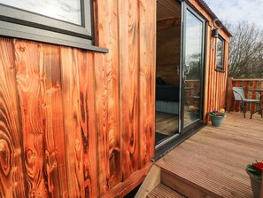 A wooden deck with a sliding glass door leading to a room with a bed and a chair. - The Bumblebee (Pembroke)