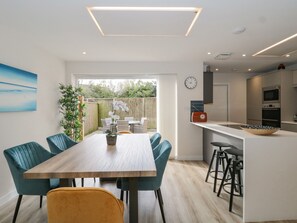 Une cuisine moderne dotée d’un îlot central, d’un coin repas avec une table et des chaises en bois, et offrant une vue sur le jardin arrière.