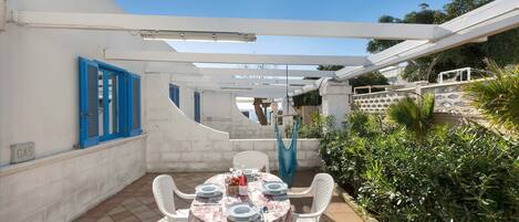 A patio with a table set for dining, white chairs, and a blue door.