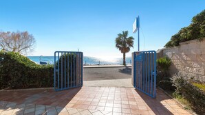 Una entrada con reja y vista al mar, una palmera y un muro de piedra.