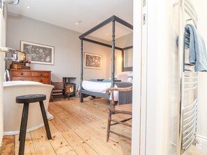 A bedroom with a four-poster bed, wooden floor, dresser, and a chair. - Treveddoe Farmhouse (Bodmin)
