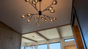 A spacious living area with a modern chandelier, large windows, and a wooden staircase. - Luxury Family and Friends Getaway, Indoor Pool, Theater, Epic Smoky Mtn Views (Sevierville)