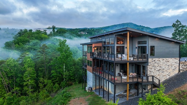 A modern two-story house with a balcony, surrounded by lush greenery and mountains. - Luxury Family and Friends Getaway, Indoor Pool, Theater, Epic Smoky Mtn Views (Sevierville)