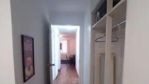 Un couloir étroit au plancher en bois, avec un porte-manteau et une porte donnant sur une autre pièce.