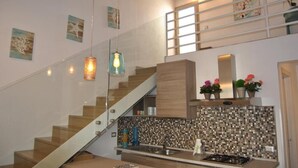 Una cocina moderna con escalera de vidrio, vigas de madera y salpicadero de azulejos.