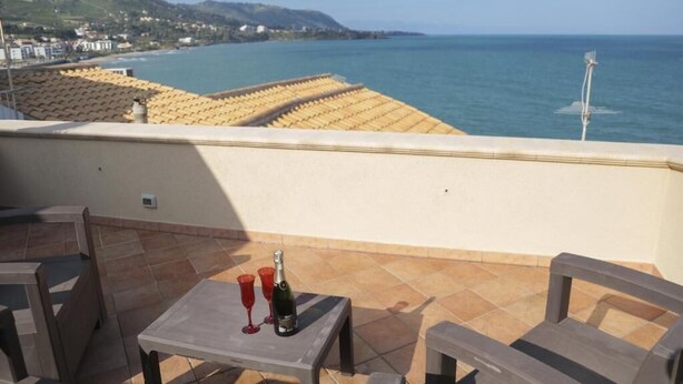 Una terraza con una mesa y sillas, con vista al litoral y edificios y colinas al fondo.