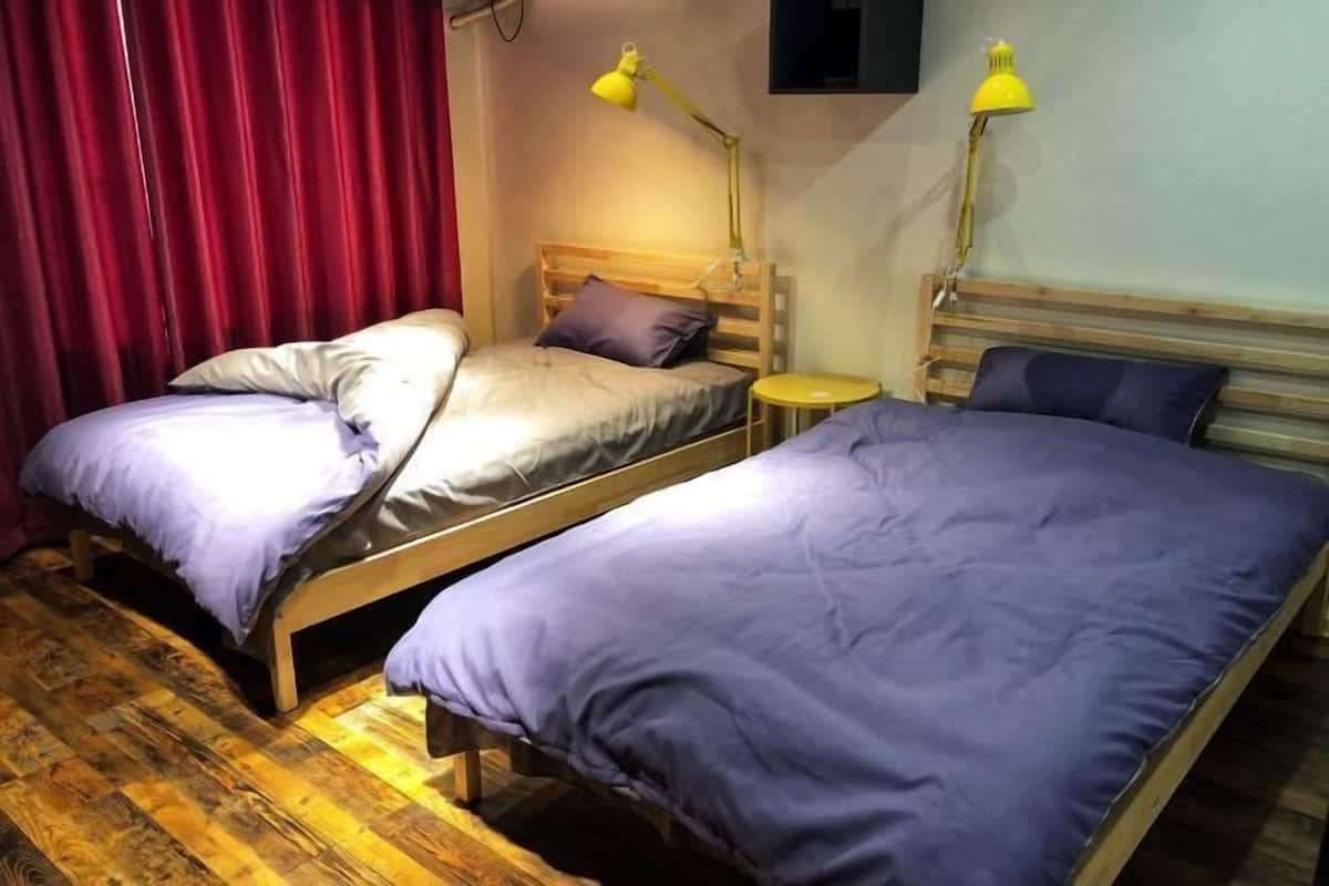 A room with two wooden beds, each with a headboard and a small bedside table. There are two yellow desk lamps on the wall above the beds.
