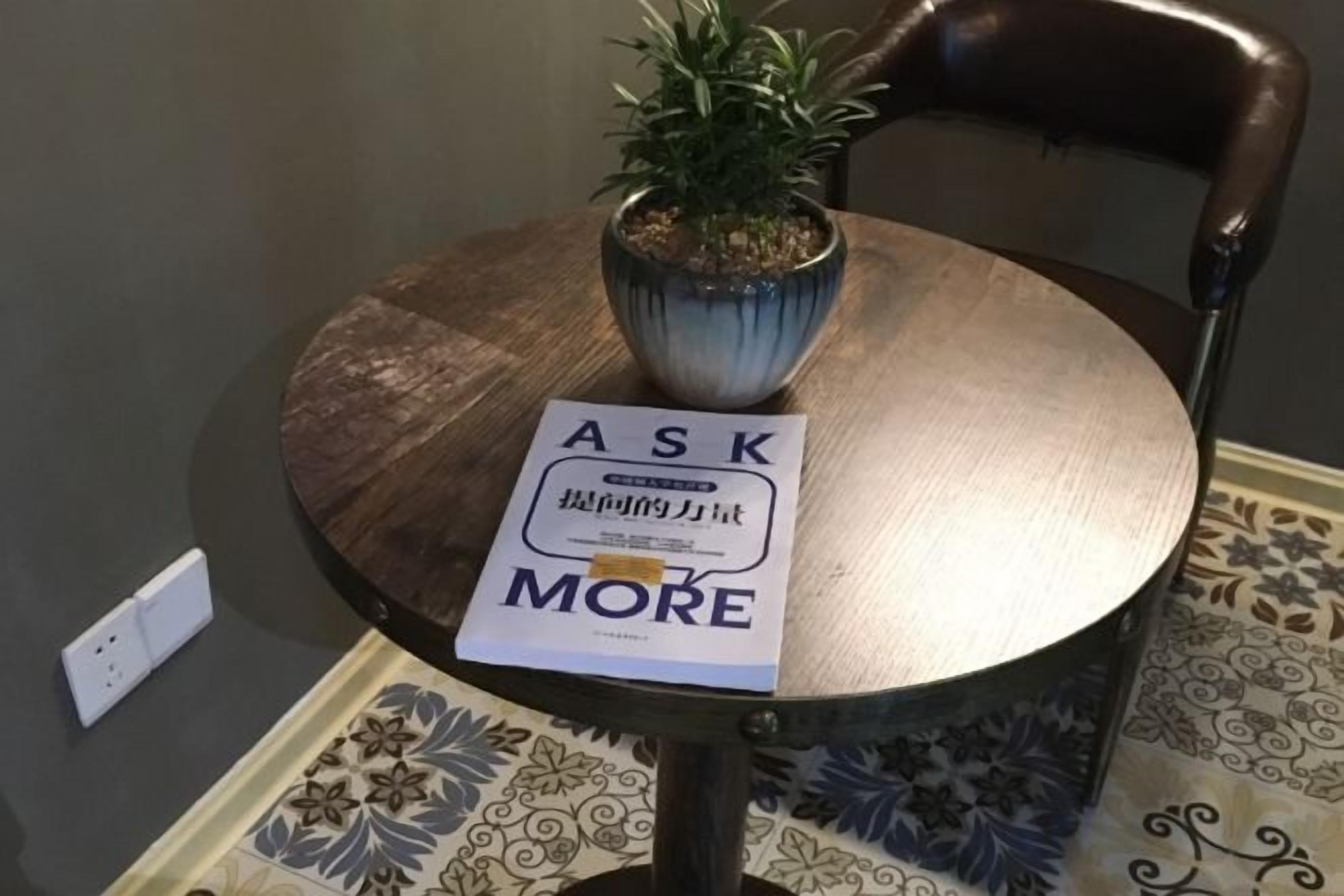 Una mesa redonda con una planta en maceta y un letrero que dice 'ASK MORE'.