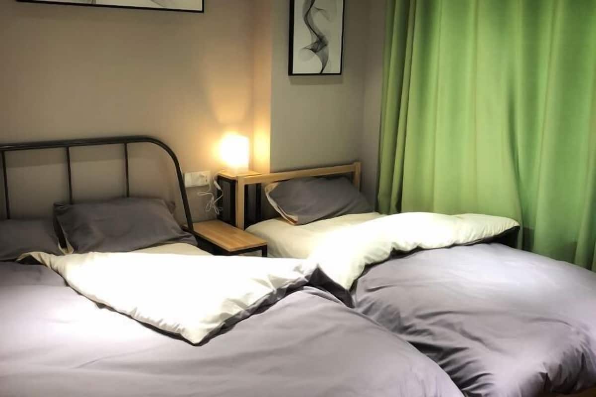 A hotel room with two beds, a bedside table with a lamp, and a green curtain.