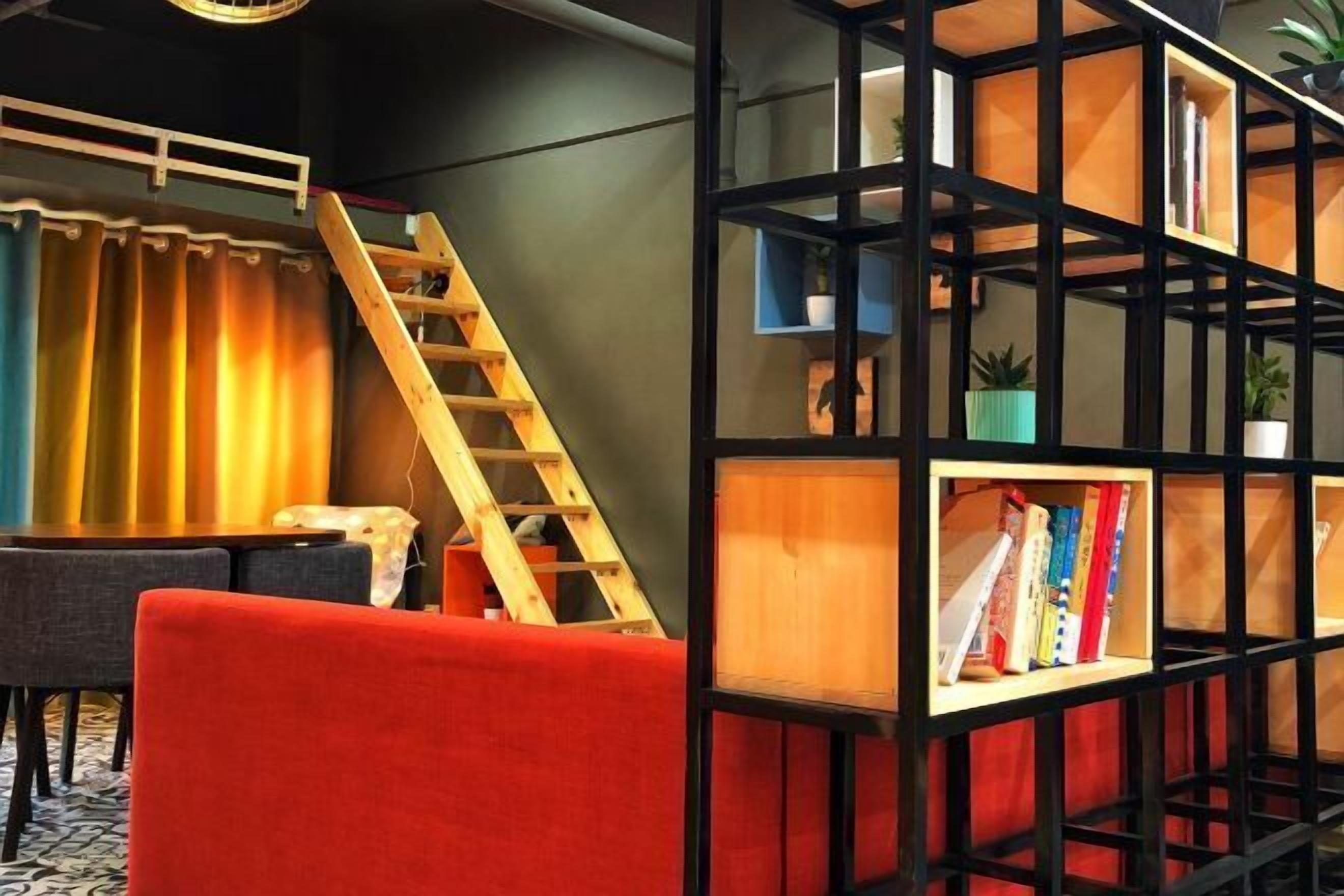 A room with a red sofa, a wooden ladder, and a black bookshelf with books and plants.