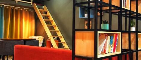 A room with a red sofa, a wooden ladder, and a black bookshelf with books and plants.
