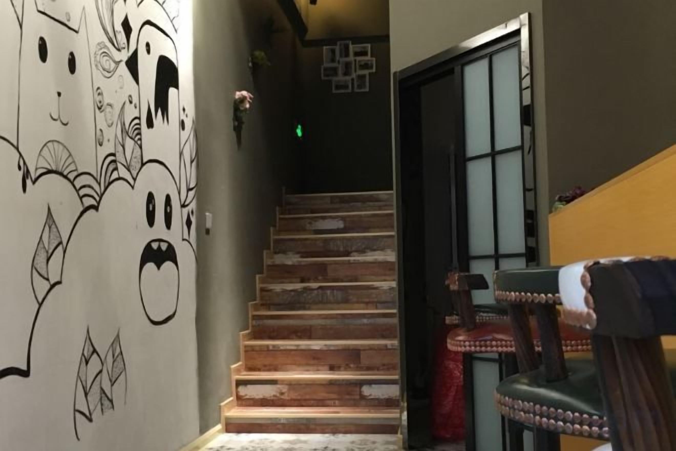 Una escalera con detalles de madera, una pared con un mural y una puerta que da a otra habitación.
