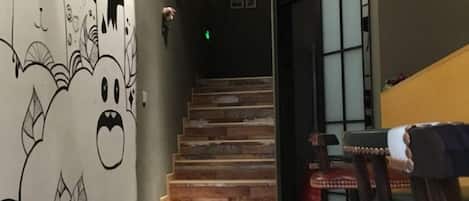 Una escalera con detalles de madera, una pared con un mural y una puerta que da a otra habitación.