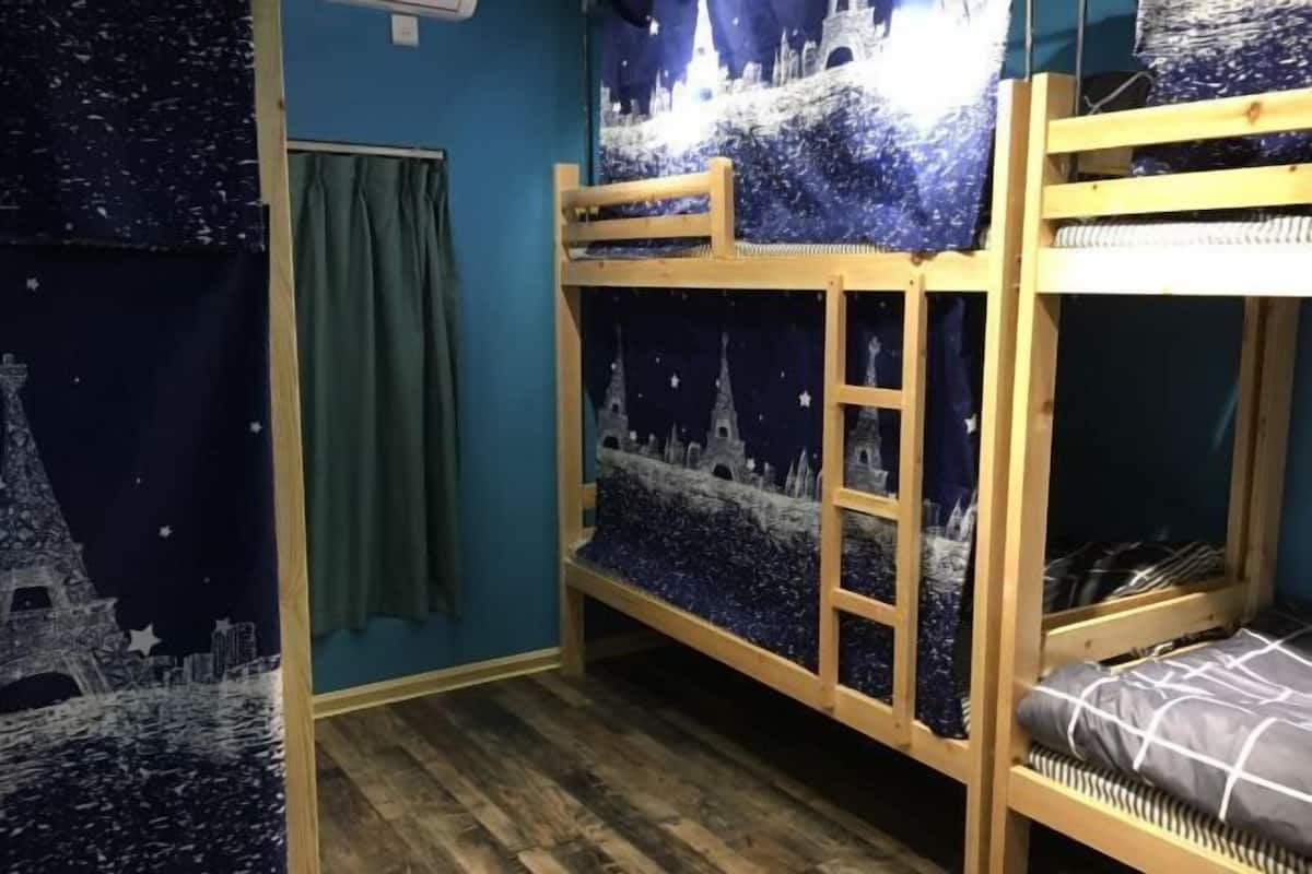 A bunk bed room with a starry night theme, wooden flooring, and a green curtain.