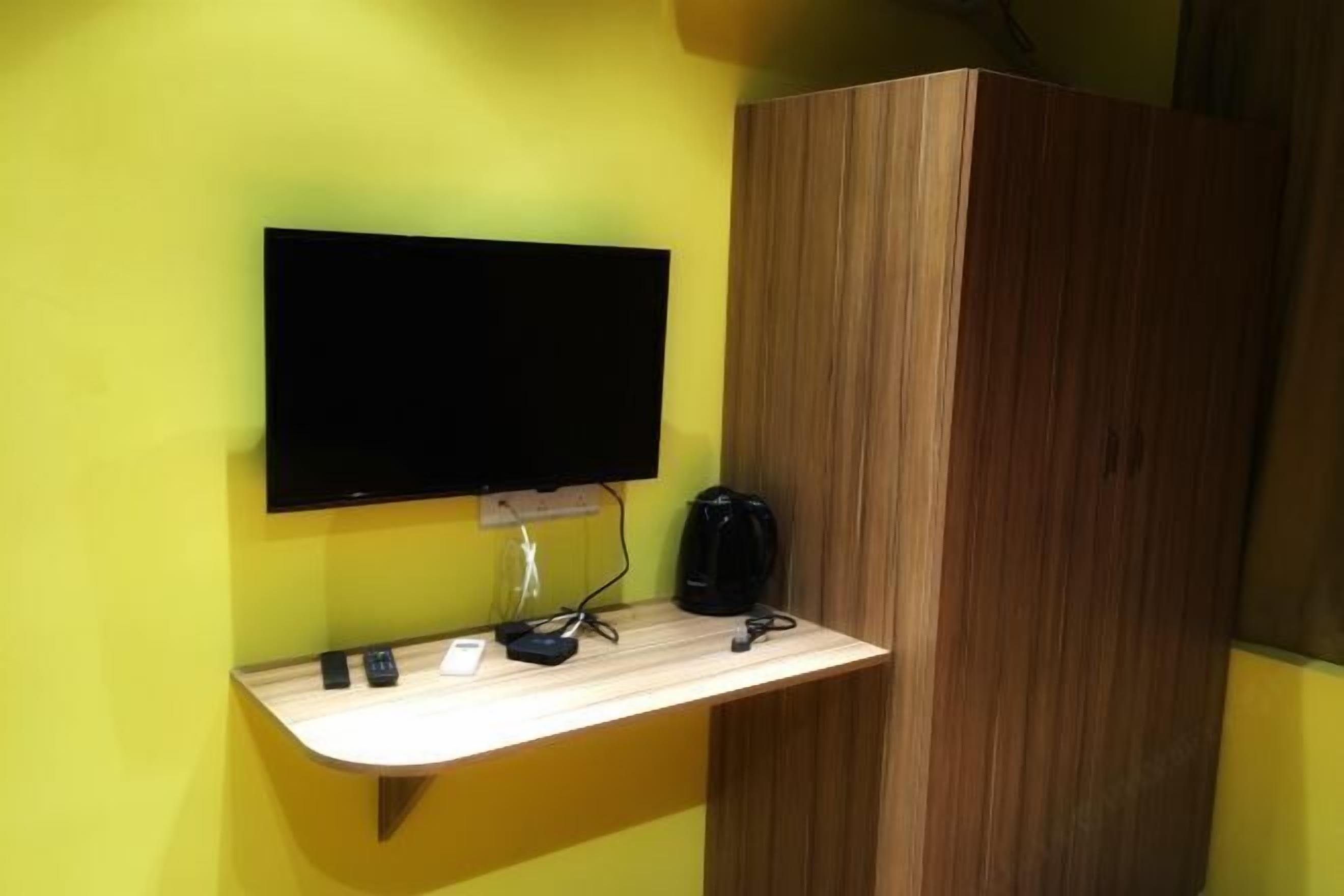 A room with a flat-screen TV mounted on a wall, a wooden cabinet, and a small wooden counter with a coffee maker and a phone.