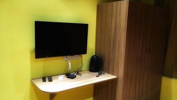 A room with a flat-screen TV mounted on a wall, a wooden cabinet, and a small wooden counter with a coffee maker and a phone.