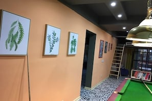 Een gang met ingelijste botanische prints aan de muur, een pooltafel en een ladder die naar een deur leidt.