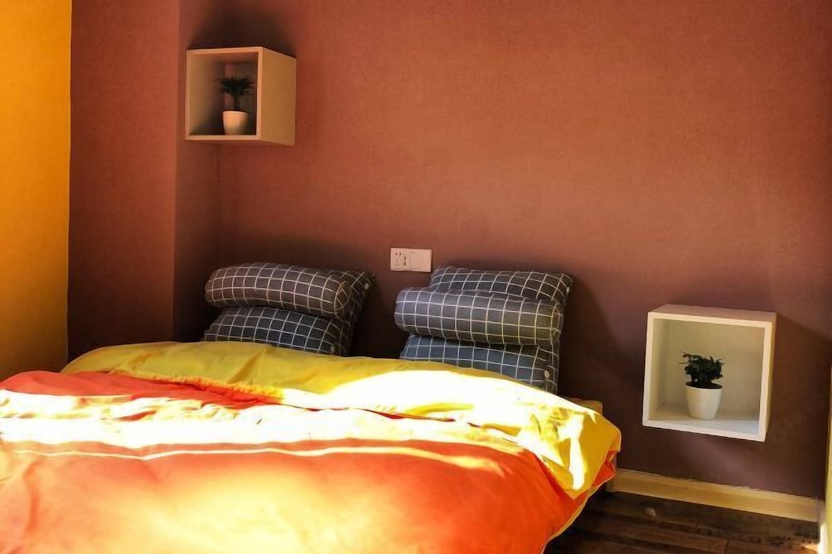 Une chambre à coucher avec un lit, des oreillers, une table de chevet avec une plante et une étagère fixée au mur.