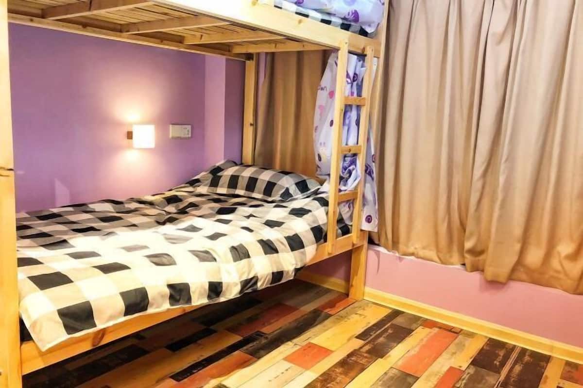 A bunk bed with a checkered bedspread, a wall-mounted light, and a wooden floor.