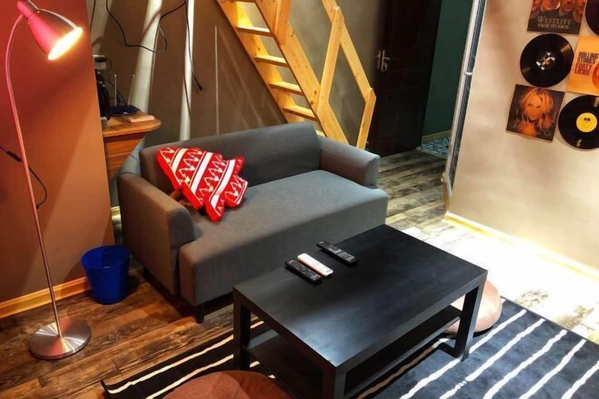 A room with a grey sofa, a black coffee table, a blue trash bin, a wooden ladder, and a wall with vinyl records.
