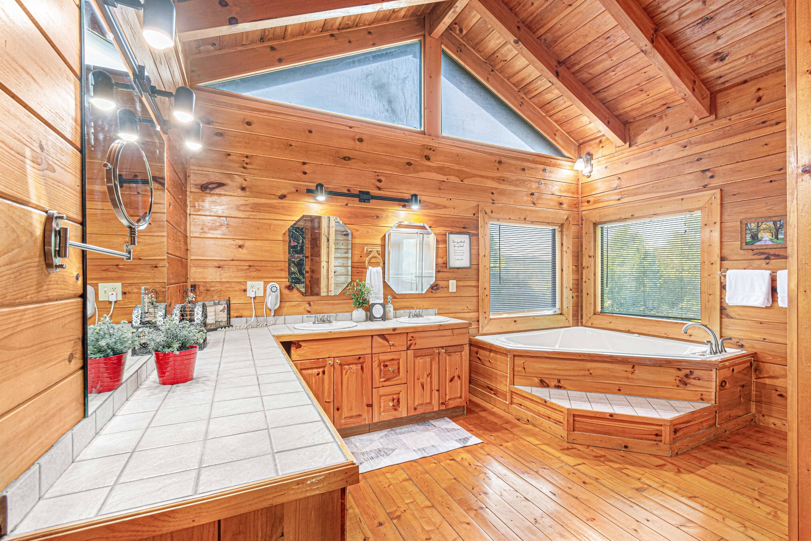A wooden cabin bathroom with a large vanity, a bathtub, and a skylight.