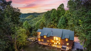 Een chalet met een veranda, omringd door dicht bos en uitzicht op de bergen achtergrond.