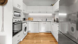 A modern kitchen with white cabinets, stainless steel appliances, and a wooden floor.