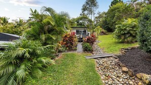 A modern house with a pathway leading to the entrance, surrounded by lush greenery and tropical plants.