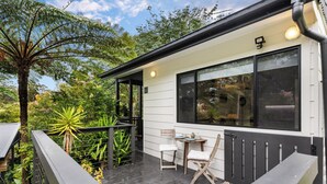 A modern house with a wooden deck, a covered outdoor seating area, and a large window overlooking a garden.