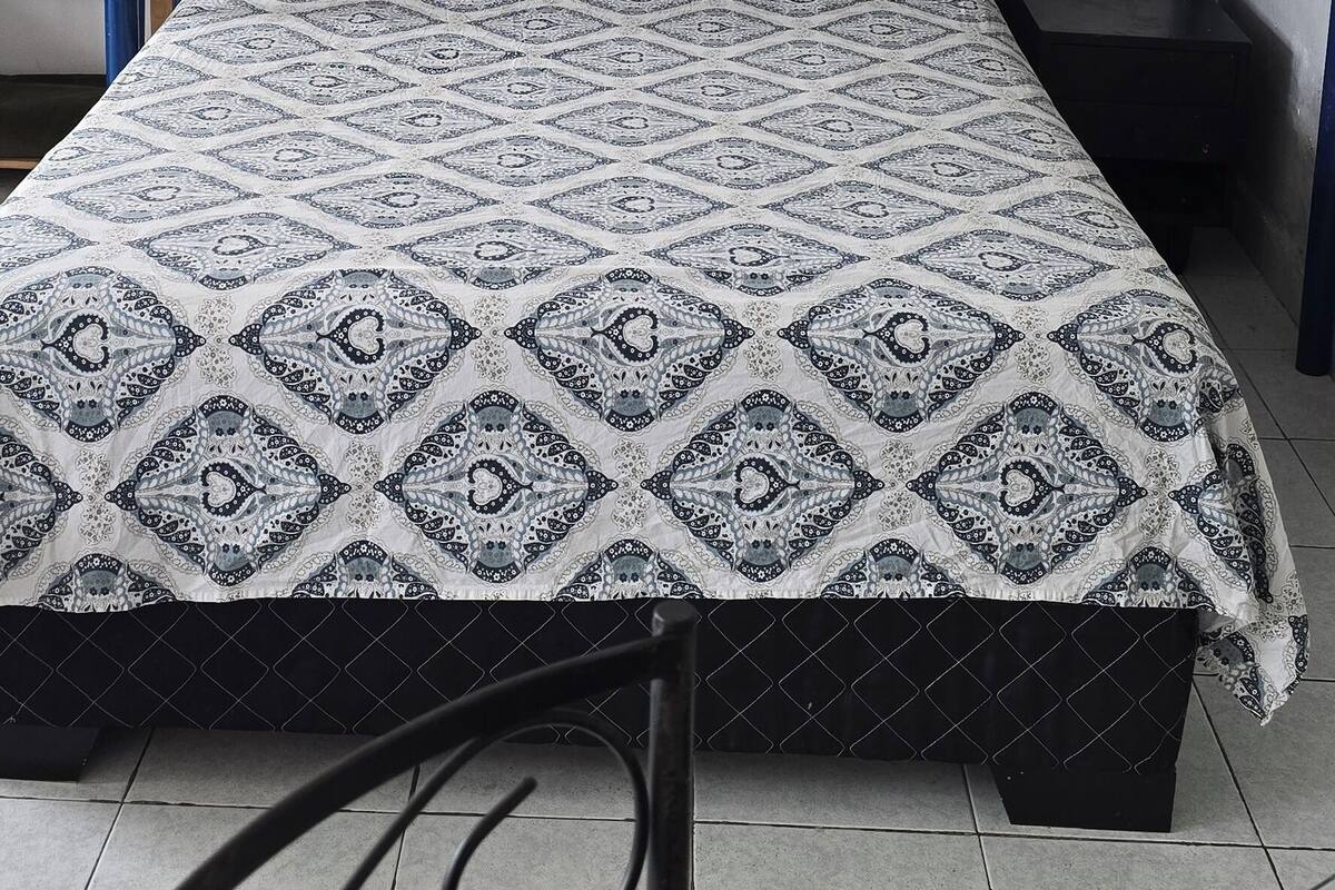 Una cama individual superpuesta con una colcha estampada, un ventilador de techo y una mesita de noche pequeña.