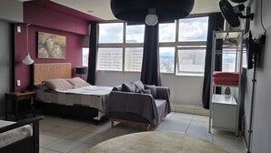 Une chambre moderne comprenant un lit, un canapé, un bureau et une grande fenêtre donnant sur la ville.