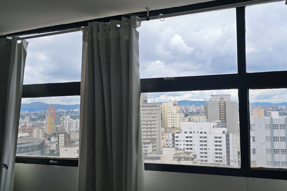 Una habitación con un amplio ventanal que ofrece vistas a un paisaje urbano con diversos edificios y montañas a lo lejos.