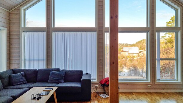 Ein modernes Interieur mit einem Ecksofa, einem Holztisch und großen Fenstern mit Blick auf eine verschneite Landschaft.
